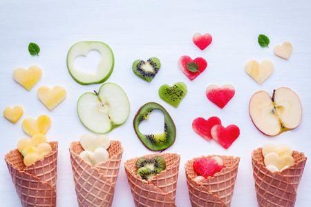 Various fruits in waffle cones and heart shape of fruits setup on white wooden backgroundの写真素材