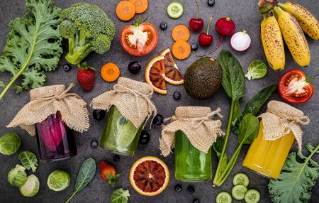 Colourful healthy smoothies and juices in bottles with fresh tropical fruit and superfoods on dark stone background with copy space.の写真素材
