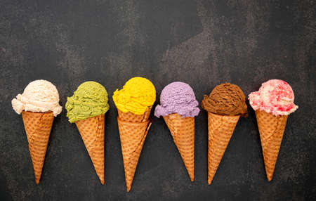 Various of ice cream flavor in cones blueberry ,green tea ,pistachio ,almond ,orange and cherry setup on dark stone background . Summer and Sweet menu concept.の写真素材
