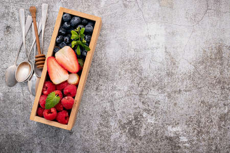 Various fresh berries blueberry, raspberry and strawberry in wooden box setup on concrete background .の写真素材