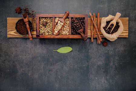 Green and brown unroasted and dark roasted coffee beans in wooden box with scoops setup on dark...