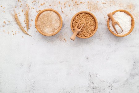 Wheat grains , brown wheat flour and white wheat flour in wooden bowl set up on white concrete background.の写真素材