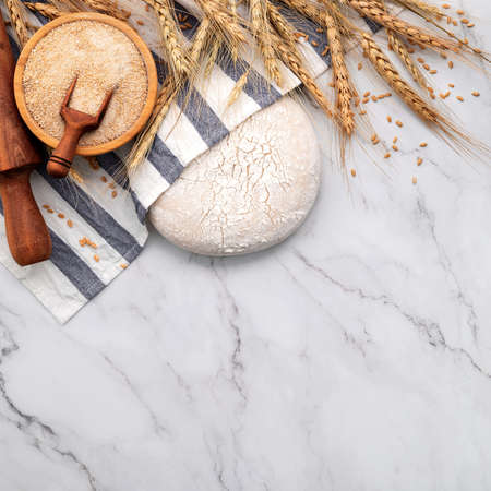 Fresh homemade yeast dough resting on marble table with ears of wheat and rolling pin.の写真素材