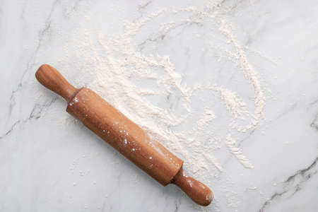 Scattered wheat flour and rolling pin set up on white marble background flat lay.の写真素材