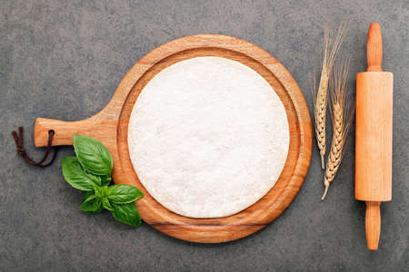 Thin homemade pizza dough with wheat ears  and rolling pin set up on dark concrete background.の写真素材