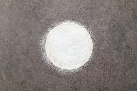 Thin homemade pizza dough with scattered wheat flour on dark concrete background.の写真素材