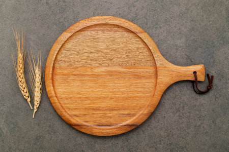 Empty wooden pizza platter with wheat ears  set up on dark concrete background.の写真素材