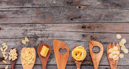 Italian foods concept and menu design . Various kind of pasta elbow macaroni ,farfalle ,rigatoni ,gnocco sardo in wooden spoons setup on wooden background.の写真素材