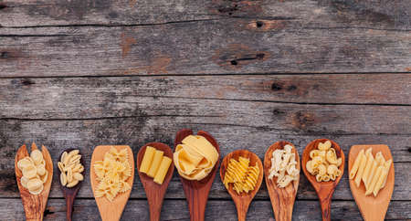 Italian foods concept and menu design . Various kind of pasta elbow macaroni ,farfalle ,rigatoni ,gnocco sardo in wooden spoons setup on wooden background.の写真素材