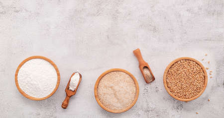 Wheat grains , brown wheat flour and white wheat flour in wooden bowl set up on white concrete background.の写真素材