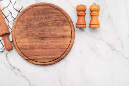 Empty wooden pizza platter with napkin and rolling pin set up on marble stone kitchen table. Pizza board and tablecloth on white marble background.の写真素材