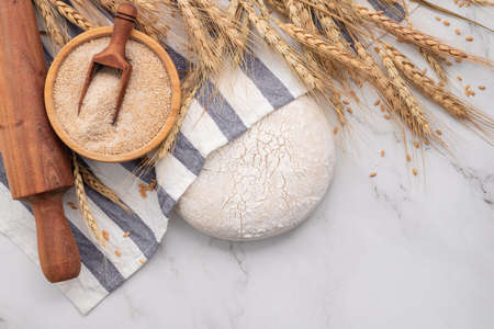 Fresh homemade yeast dough resting on marble table with ears of wheat and rolling pin.の写真素材