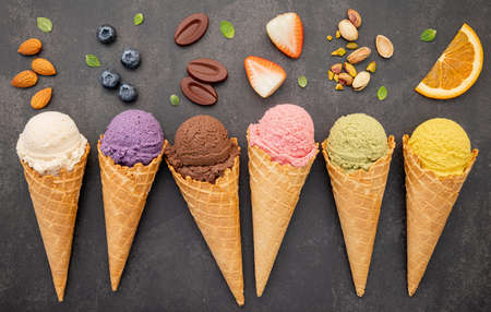 Various of ice cream flavor in cones blueberry ,pistachio ,almond ,orange and chocolate setup on dark stone background . Summer and Sweet menu concept.の写真素材