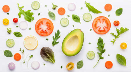Food pattern with raw ingredients of salad, lettuce leaves, cucumbers, tomatoes, carrots, broccoli, basil ,onion and lemon flat lay on white wooden background.の写真素材