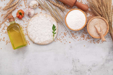 The ingredients for homemade pizza dough with wheat ears ,wheat flour and wheat grains set up on white concrete background.の写真素材