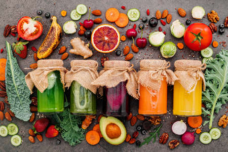 Colourful healthy smoothies and juices in bottles with fresh tropical fruit and superfoods on dark stone background with copy space.の写真素材