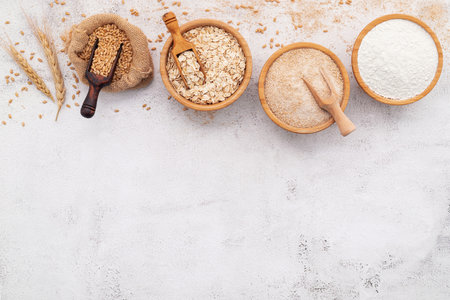 Wheat grains , brown wheat flour and white wheat flour in wooden bowl set up on white concrete background.の写真素材