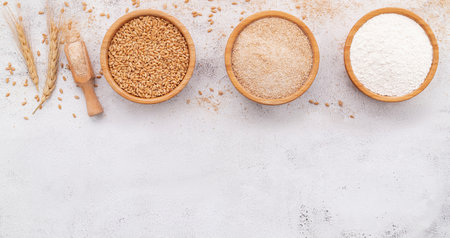 Wheat grains , brown wheat flour and white wheat flour in wooden bowl set up on white concrete background.の写真素材