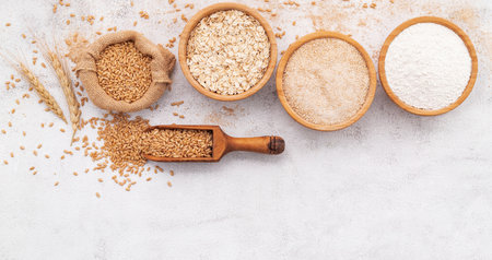 Wheat grains , brown wheat flour and white wheat flour in wooden bowl set up on white concrete background.の写真素材