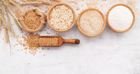 Wheat grains , brown wheat flour and white wheat flour in wooden bowl set up on white concrete background.の写真素材