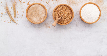 Wheat grains , brown wheat flour and white wheat flour in wooden bowl set up on white concrete background.の写真素材