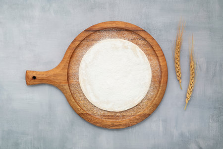 Homemade pizza dough in wooden pizza platter with wheat ears set up on grey concrete background flat lay and copy spaceの写真素材