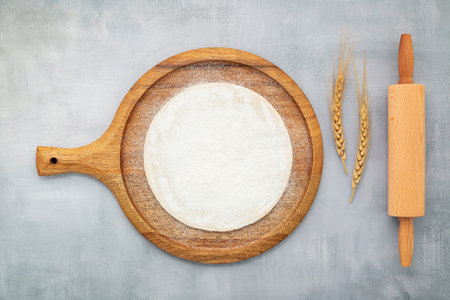Homemade pizza dough in wooden pizza platter with wheat ears set up on grey concrete background flat lay and copy spaceの写真素材