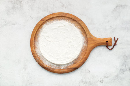 Pizza dough in wooden pizza platter set up on white concrete. Pizza tray on white concrete background flat lay and copy space.の写真素材