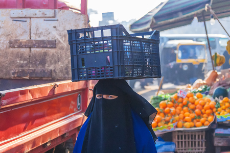 Woman in niqab carries a box on her head with vegetables, egyptian people on streetのeditorial素材