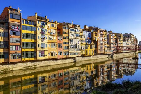 Colorful yellow and orange houses reflected in water river Onyar, in Girona. Cathedral of Girona at background, famous landmarks of Girona, Catalonia, Spain.の写真素材