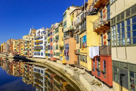 Colorful yellow and orange houses reflected in water river Onyar, in Girona. Cathedral of Girona at background, famous landmarks of Girona, Catalonia, Spain.の写真素材
