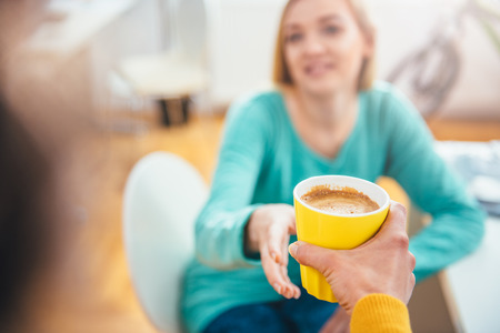 Woman giving yellow coffee cup to her colleague in the officeの写真素材