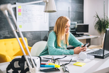 Business woman using smart phone and sitting at the desk in the officeの写真素材