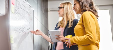 Two business woman discussing in front of the whiteboard in the officeの写真素材