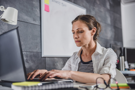 Woman wearing white shirt using laptop at officeの写真素材