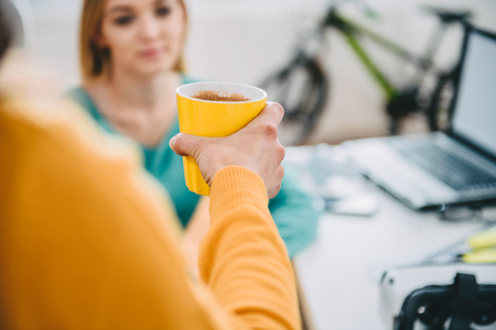 Woman giving yellow coffee cup to her colleague in the officeの写真素材