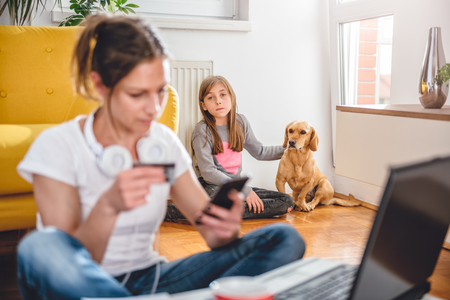 Lonely and sad daughter sitting with dog and seek attention while mother shopping online and using smart phoneの写真素材