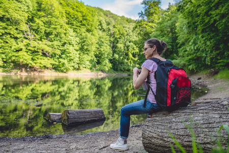 Woman sitting on a tree log by the lake and holding water bottleの写真素材