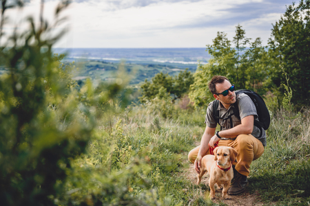 Man wearing sunglasses with a small yellow dog resting at the hiking trailの写真素材