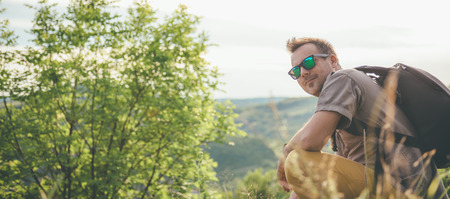 Man wearing sunglasses and backpack resting on the meadow and looking backの写真素材