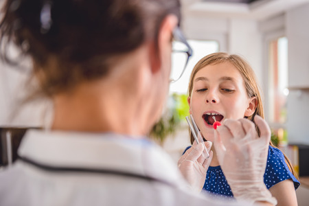 Female pediatrician using a swab to take a sample from a patient's throatの写真素材