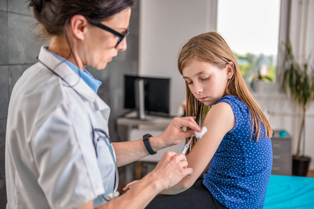 Pediatrics female doctor giving a young girl a vaccine shot in the armの写真素材