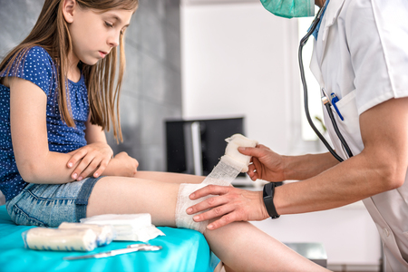 Medical female doctor bandaging young girl knee at the hospitalの写真素材