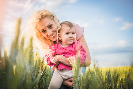 Happy mother holding her baby girl her arms in the wheat fieldの写真素材