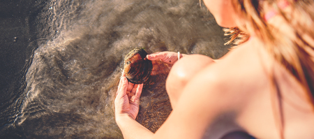Girl playing with the shell in shallow water on the beachの写真素材