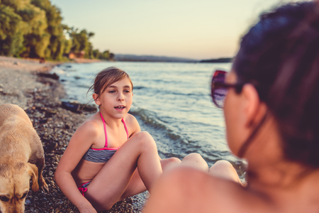 Mother and daughter sitting and talking on the beachの写真素材
