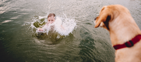 Girl swimming in river and dog standing on the dockの写真素材
