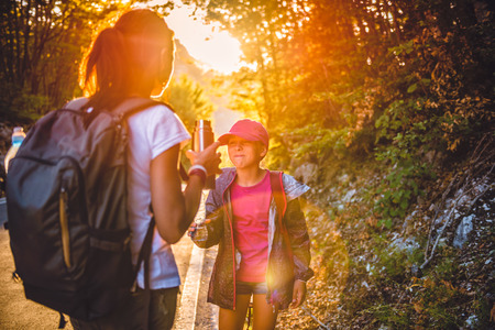 Mother and daughter hiking by the asphalt road in the forestの写真素材
