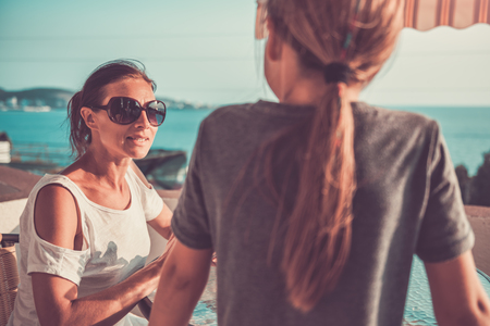Mother wearing sunglasses talking with daughter on balconyの写真素材