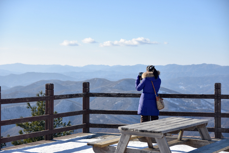 Woman looking at the mountain at winter from pier. Dressed in black jacket with hoodの写真素材